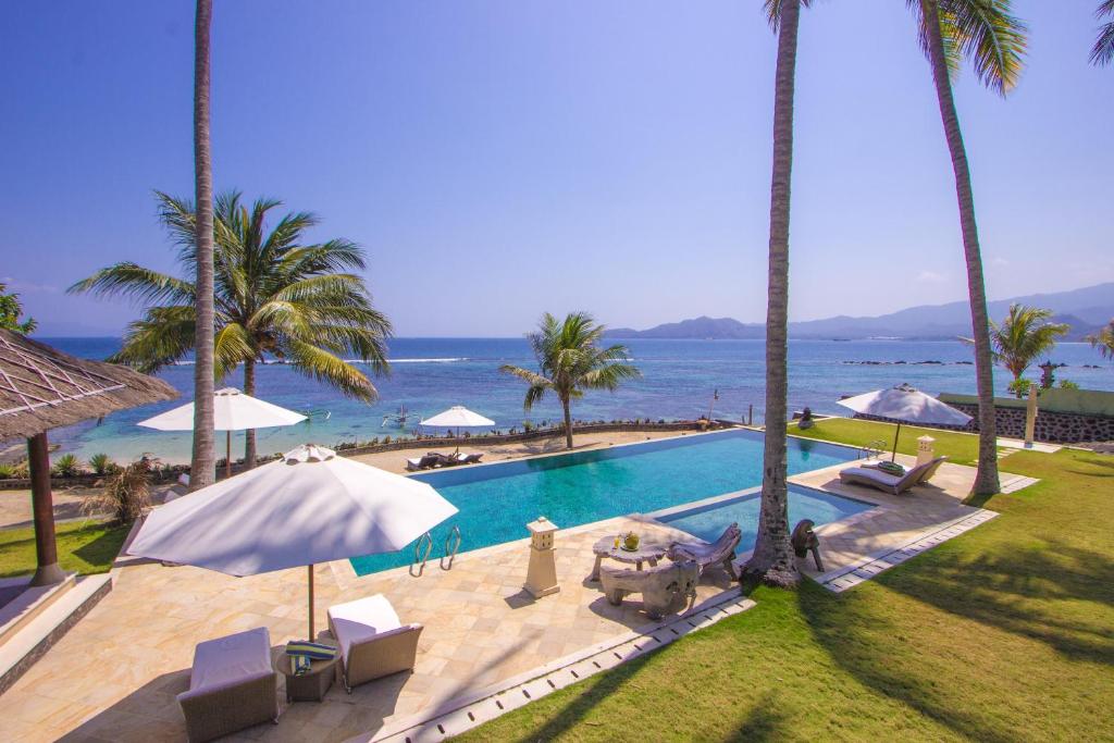 a swimming pool with palm trees and the ocean at Citakara Sari Villas in Candidasa