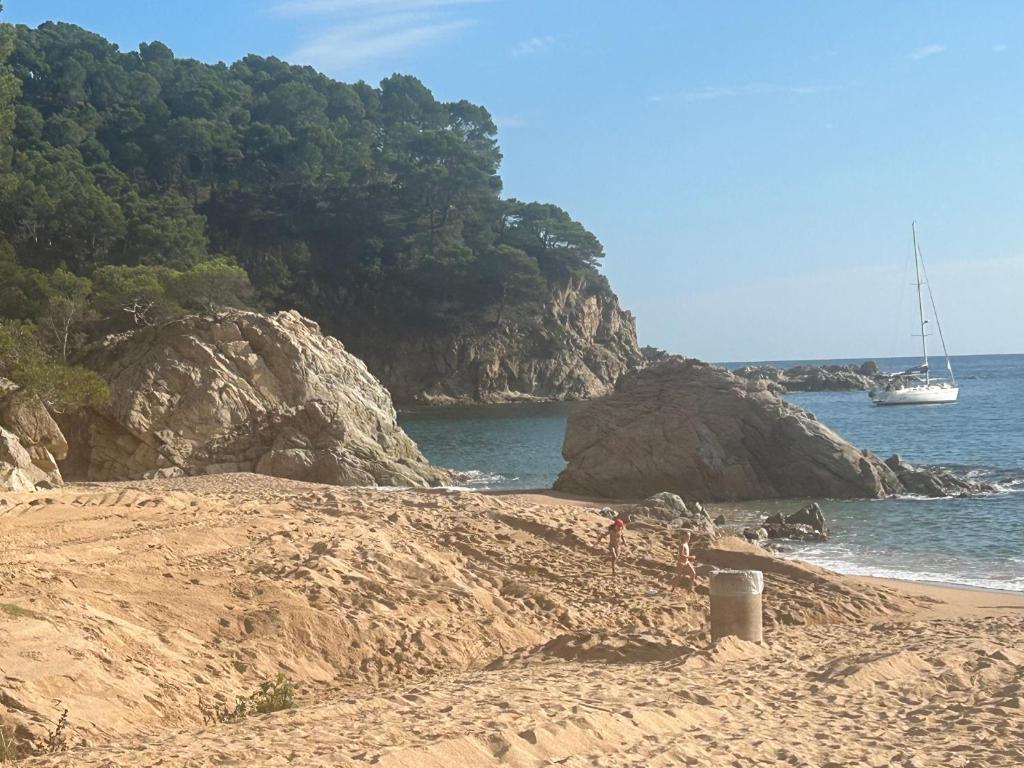 a sandy beach with a sail boat in the water at Canyelles BBQ Apartment in Lloret de Mar