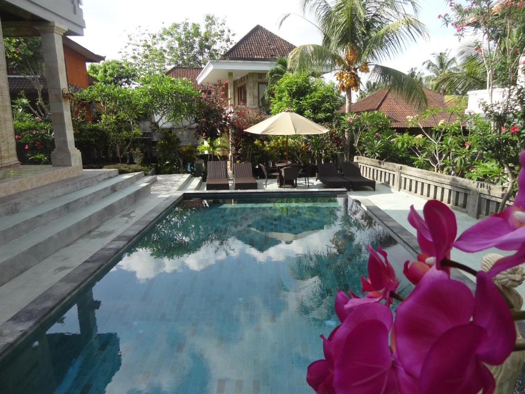 a swimming pool in front of a house with purple flowers at Kartika Bungalows in Ubud