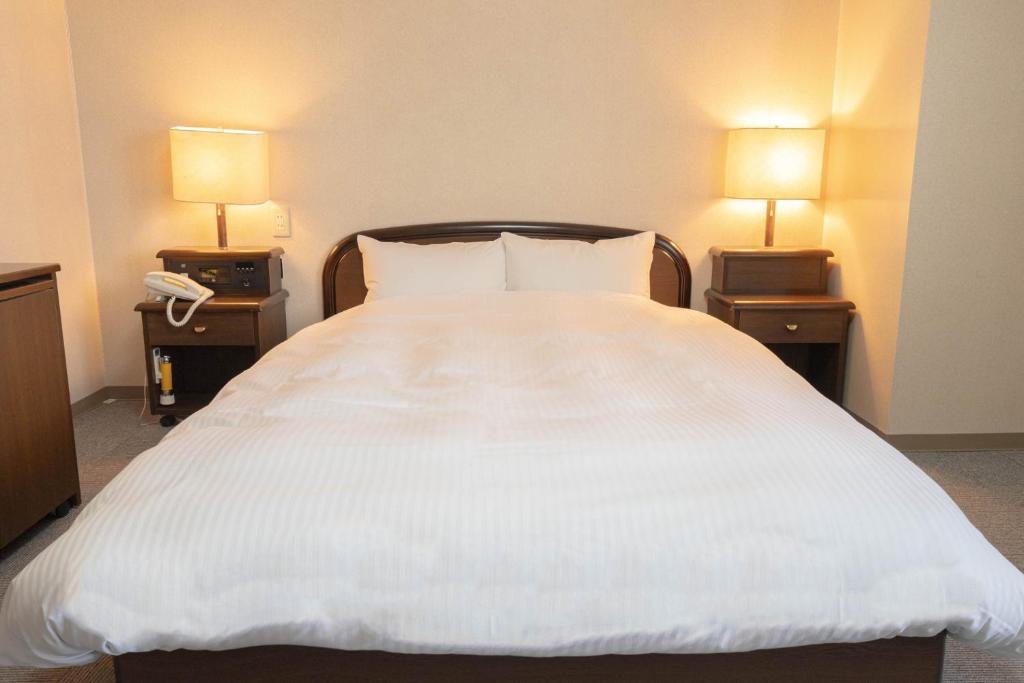 ein großes weißes Bett in einem Hotelzimmer mit zwei Lampen in der Unterkunft Hotel Alpha Inn Akita - Vacation STAY 67293v in Akita