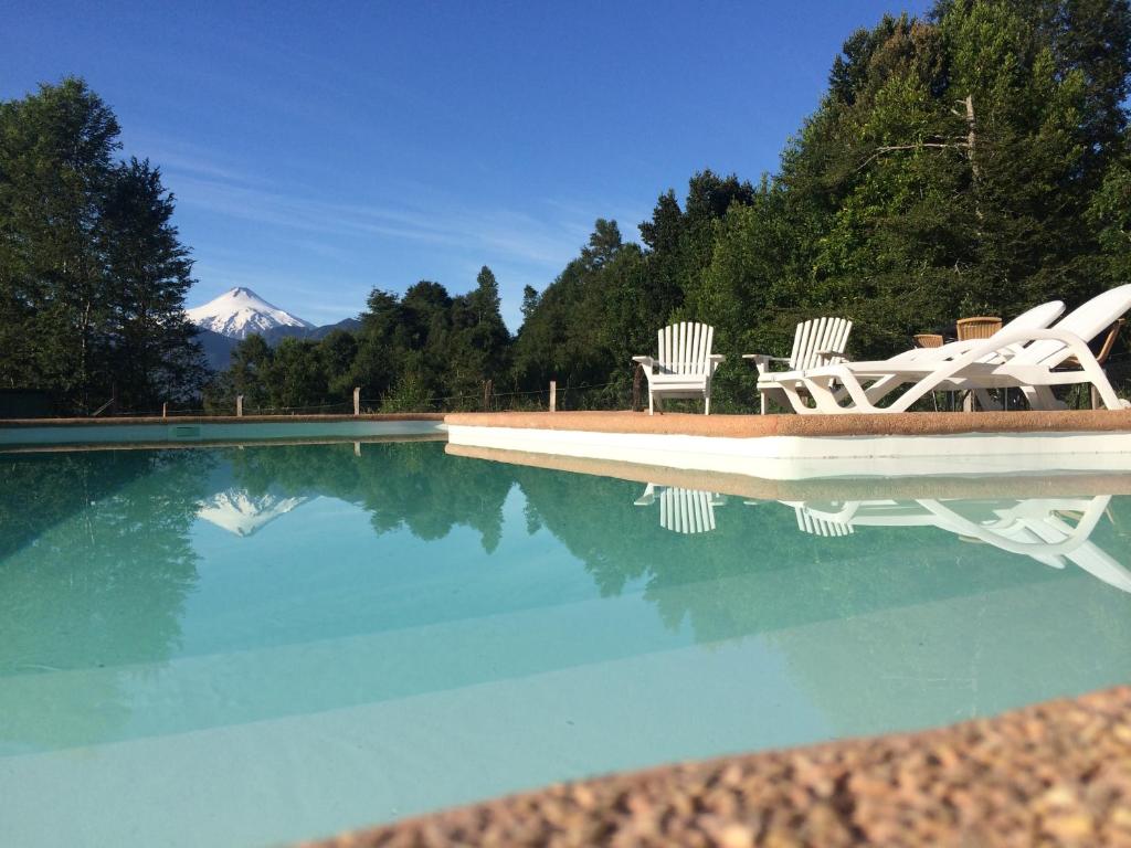 a pool with two chairs and a mountain in the background at Ecoreserva Quelhue Lodge y Cabañas in Pucón