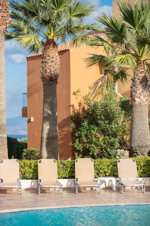 a group of chairs and palm trees next to a pool at Dia Apartments in Hersonissos