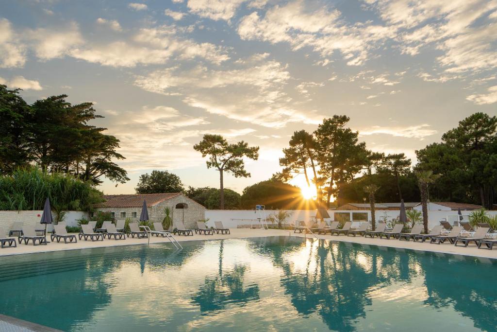 a swimming pool with chairs and the sun setting at Hôtel Les Grenettes in Sainte-Marie-de-Ré