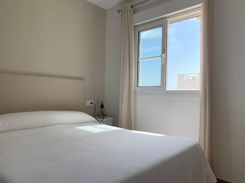 a white bedroom with a bed and a window at Apartahotel Vistamar San José in San José