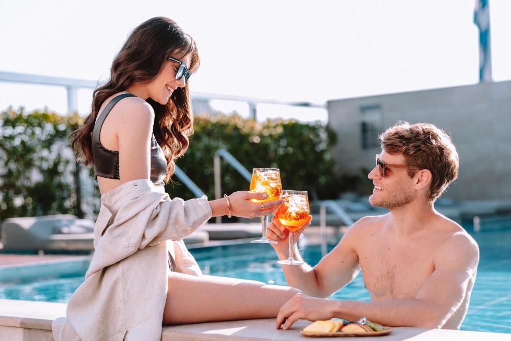 a man and a woman holding drinks near a swimming pool at Electra Metropolis in Athens
