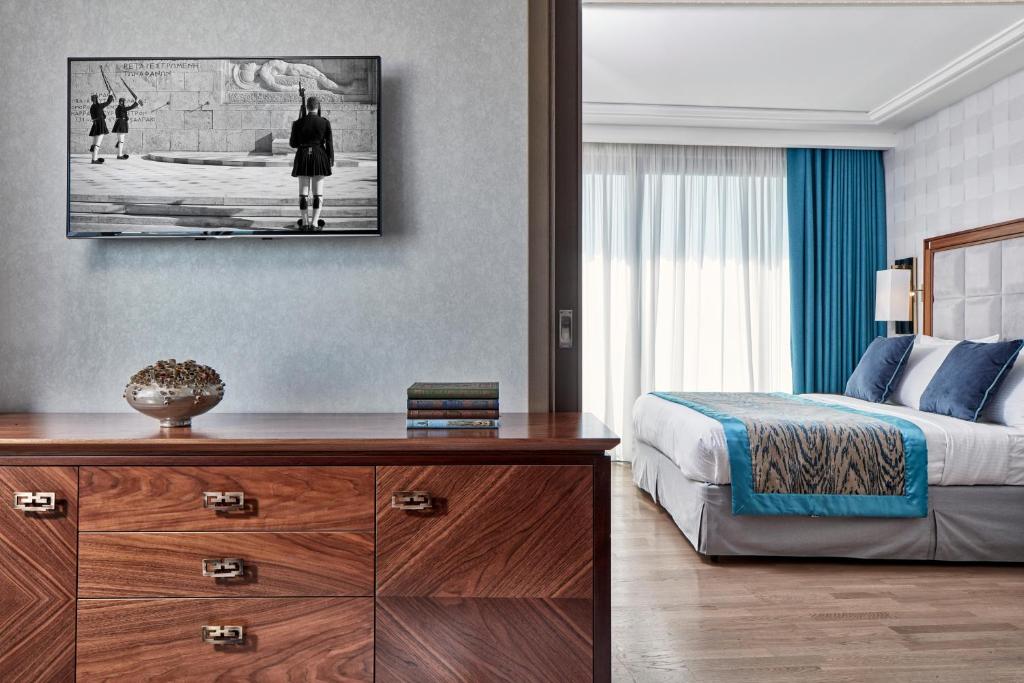 a bedroom with a bed and a wooden dresser with a desk at Electra Metropolis in Athens