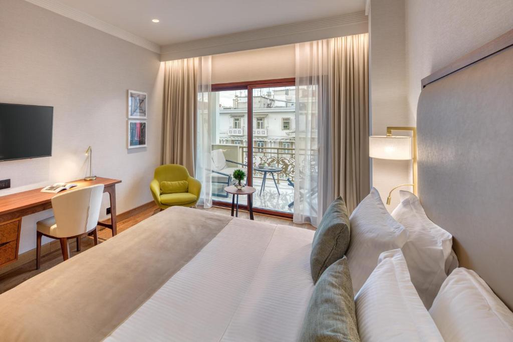 a hotel room with a bed and a desk and a window at Electra Palace Thessaloniki in Thessaloniki