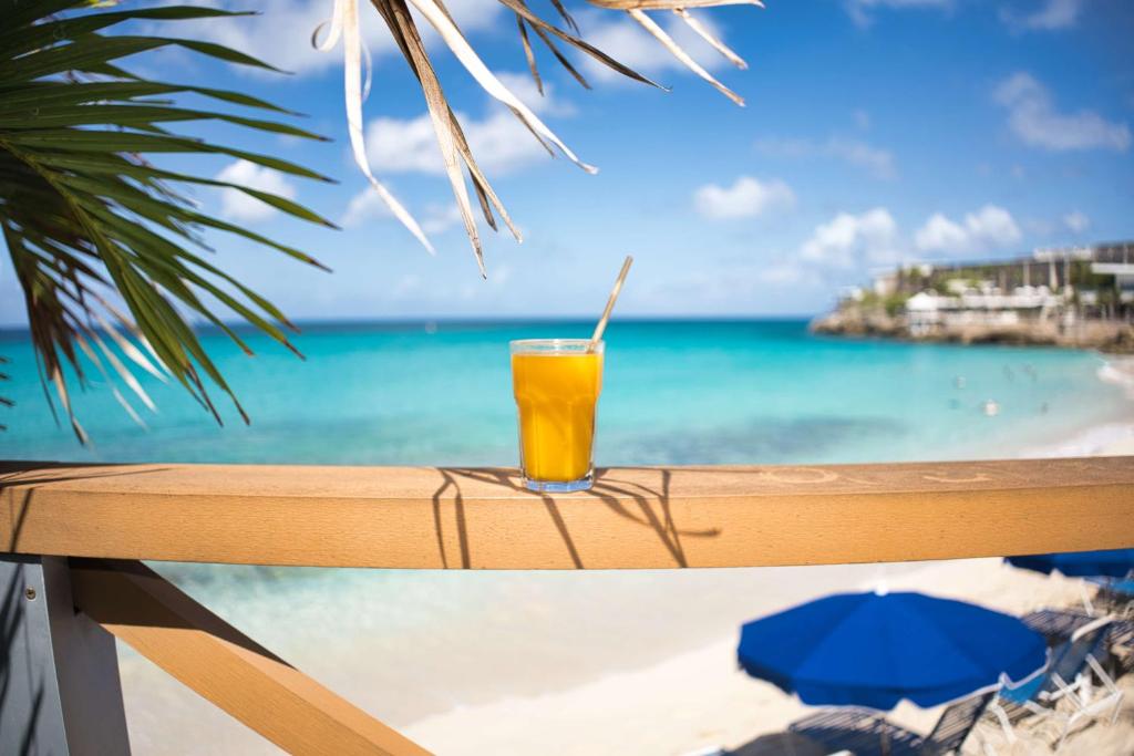 a glass of orange juice sitting on a railing overlooking the ocean at Royal Islander Club Resort La Plage in Lowlands