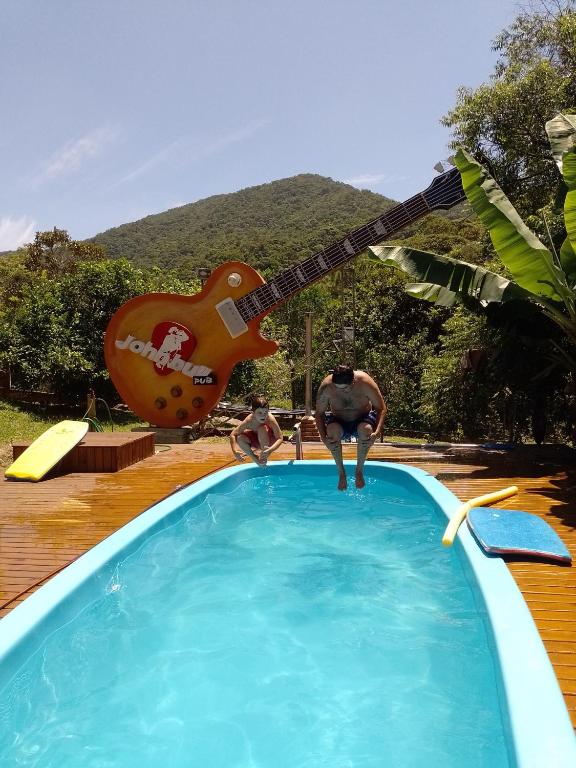 two men in a swimming pool with a guitar sign at Sítio com piscina em Caldas da Imperatriz in Santo Amaro da Imperatriz