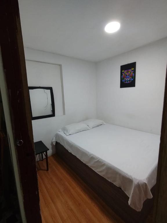 a bedroom with a white bed and a small window at Hostal la 18 in Pereira