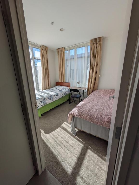 オークランドにあるNewmarket Homestay - Twin Roomのベッドルーム1室(ベッド2台、テーブル、窓付)
