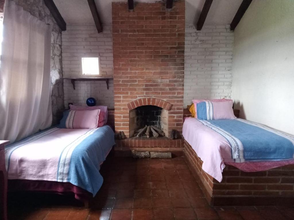 two beds in a room with a brick fireplace at Cabaña de los Sentidos in Tzintzuntzán