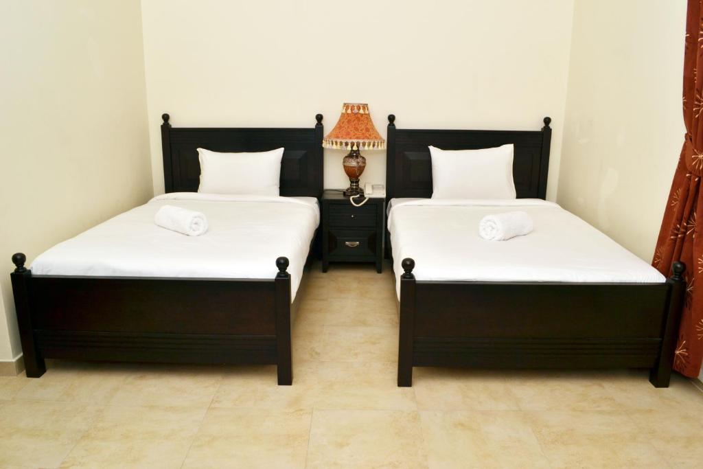 two twin beds in a room with a lamp at Sara Hotel Apartments in Ajman 