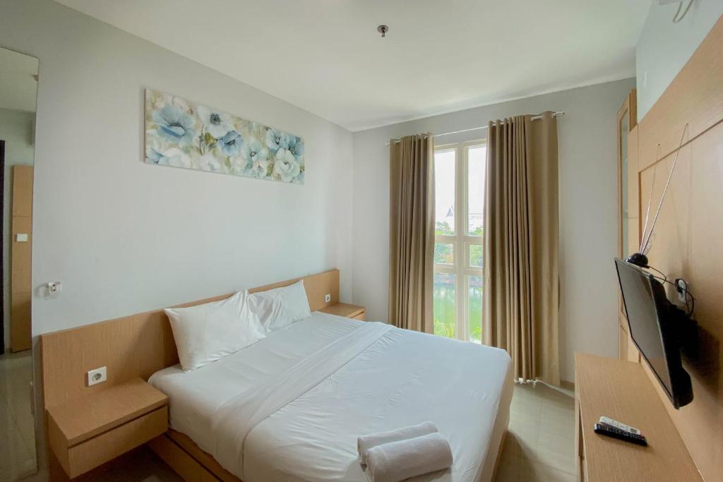 a bedroom with a white bed and a television at Best Deal and Comfort 1BR at Citralake Suites Apartment By Travelio in Jakarta