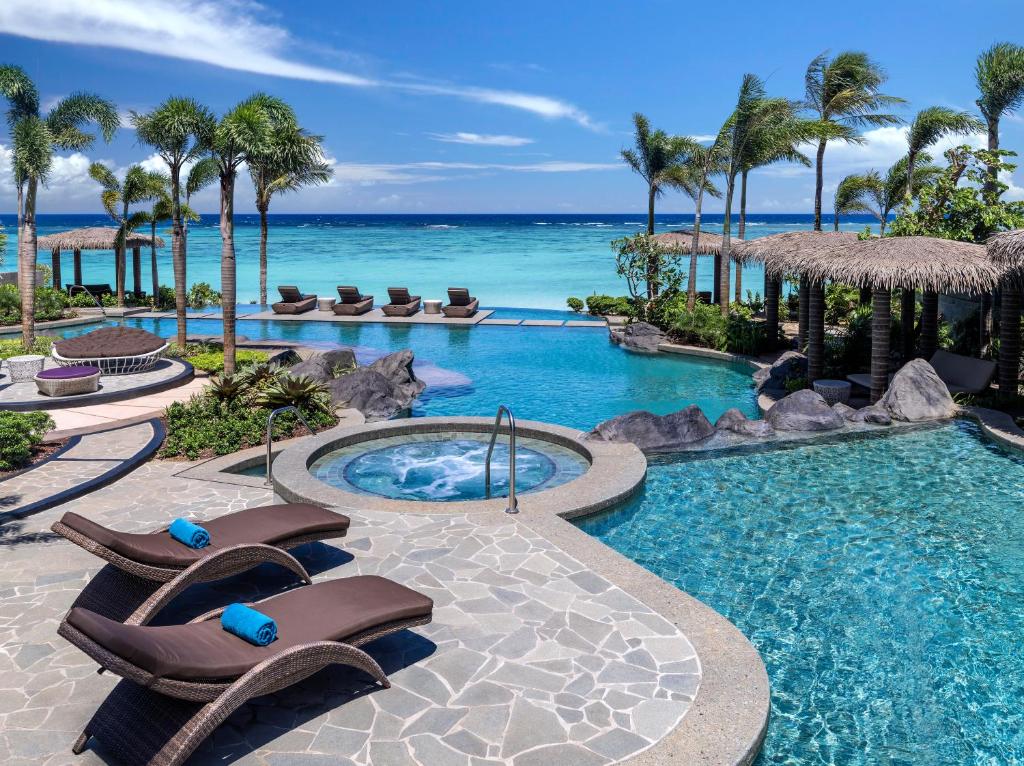 a resort swimming pool with chaise lounge chairs and the ocean at Dusit Thani Guam Resort in Tumon