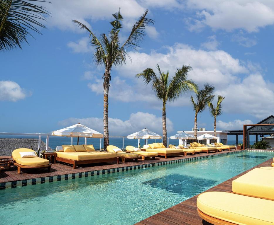a swimming pool with lounge chairs and palm trees at Secana Beachtown Resort & Residences in Canggu