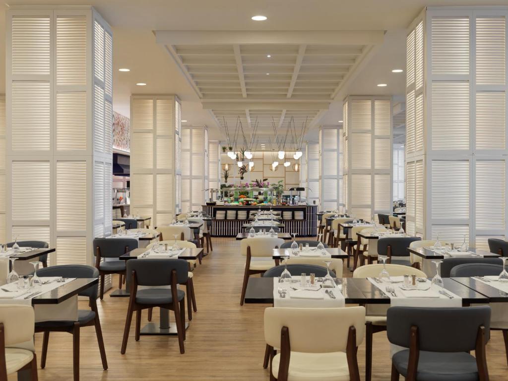 a dining room with tables and chairs and windows at H10 Estepona Palace in Estepona
