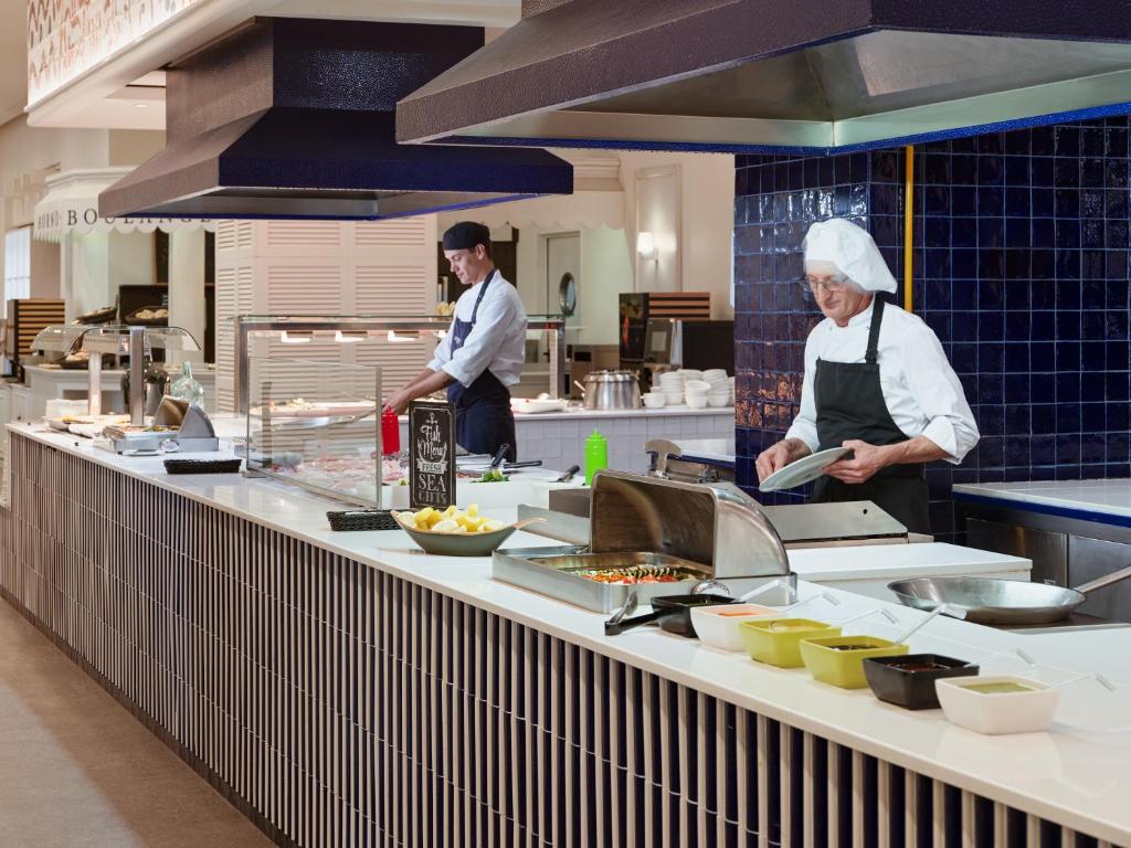 two chefs standing in a kitchen preparing food at H10 Estepona Palace in Estepona