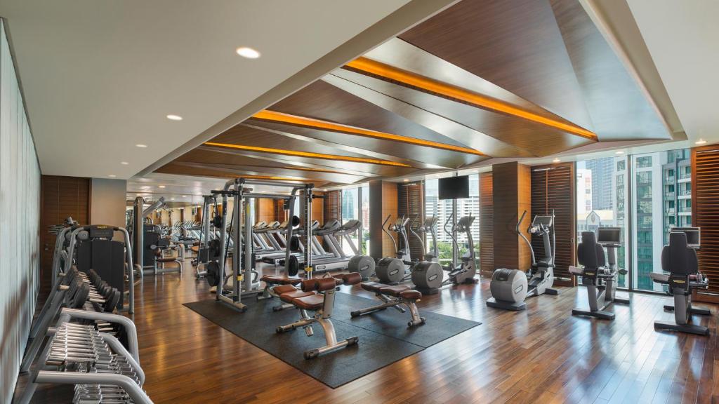 A spacious, bright fitness room contains cardio machines, strength equipment, and free weights beside large windows.