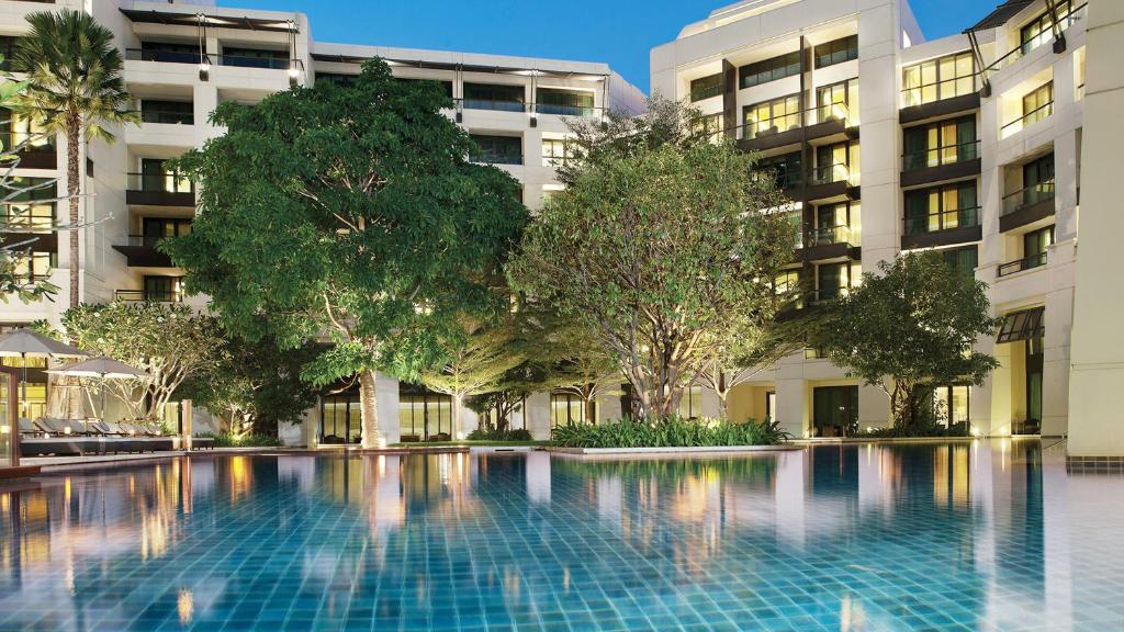 A large blue-tiled pool sits in a landscaped courtyard surrounded by hotel buildings.
