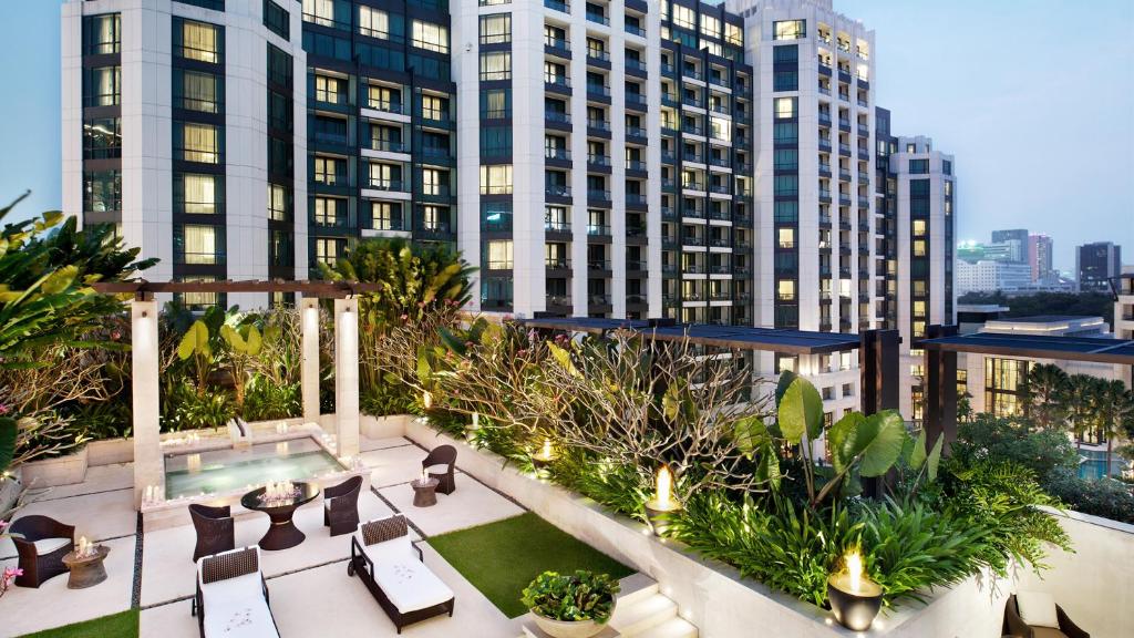 A landscaped rooftop terrace with loungers, café tables and a swimming pool overlooking Bangkok buildings.