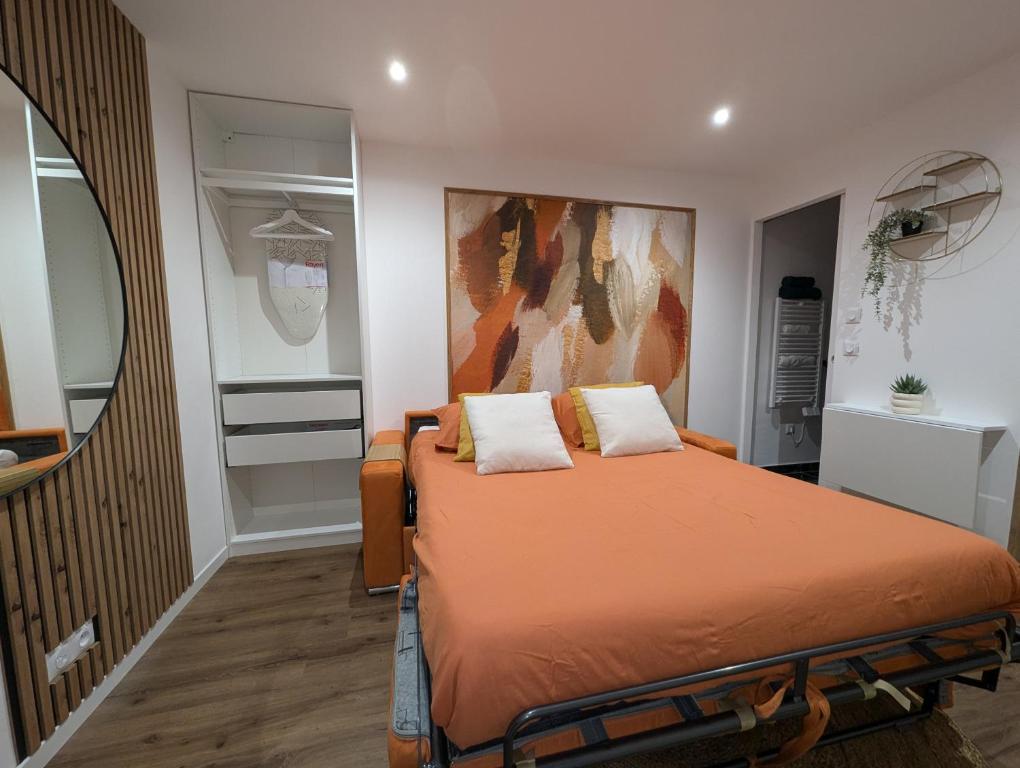 1 dormitorio con 1 cama con sábanas de color naranja y espejo en Évasion Douceur, studio accueillant, près de Paris, en Villejuif