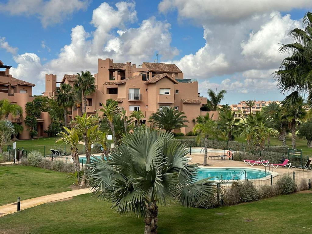 a large apartment building with a swimming pool and a palm tree at Mar Menor Golf Resort 2 Bed Apartment in Los Martínez