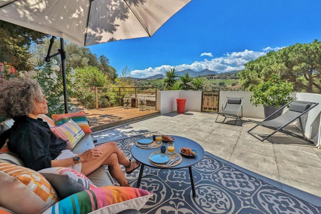 une femme assise sur un patio avec un parasol dans l'établissement Casa Albera N1 des Villages préférés des Français, à Collioure