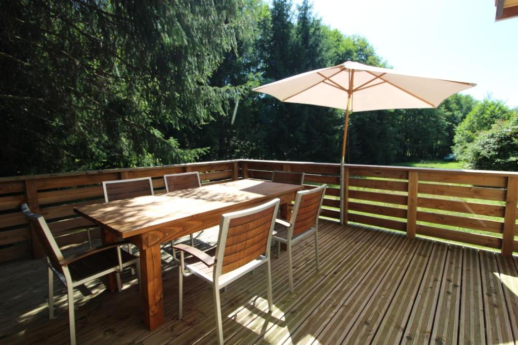 une table en bois avec un parasol sur une terrasse dans l'établissement Gîte à Rufus, Maison de charme au Ménil, au cœur de la nature vosgienne, à Le Ménil