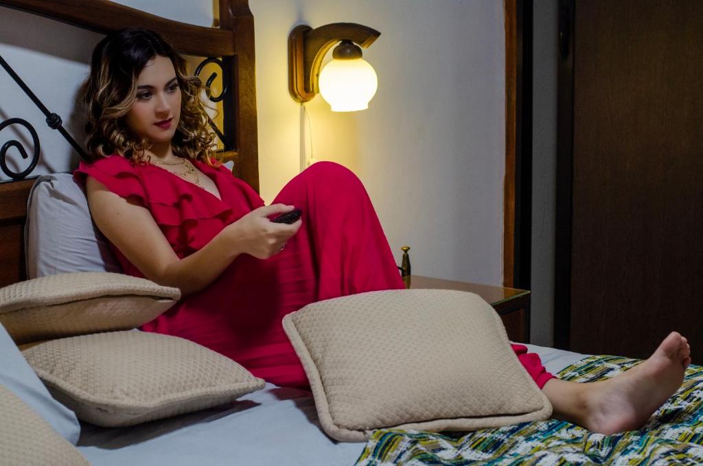 una mujer sentada en una cama sosteniendo un mando a distancia en HOTEL BOUTIQUE EL RANCHO OLIVO, en Villamontes