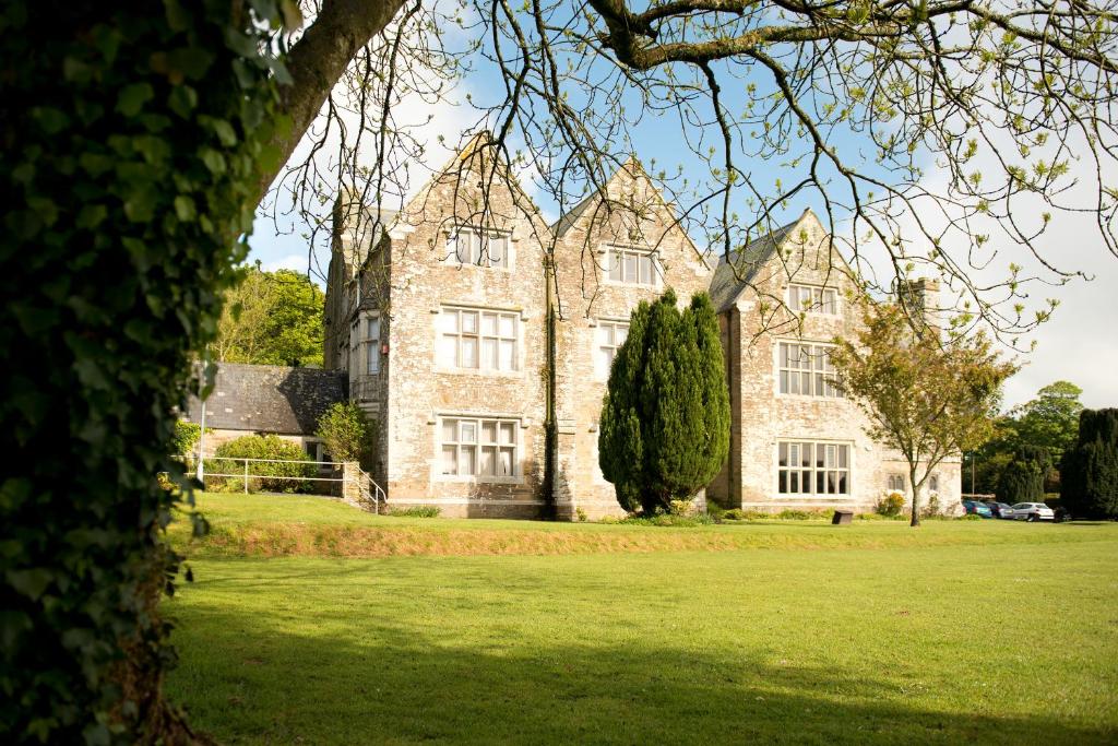 un grande edificio in pietra con un albero di fronte di Trelawne Manor Holiday Park a Looe