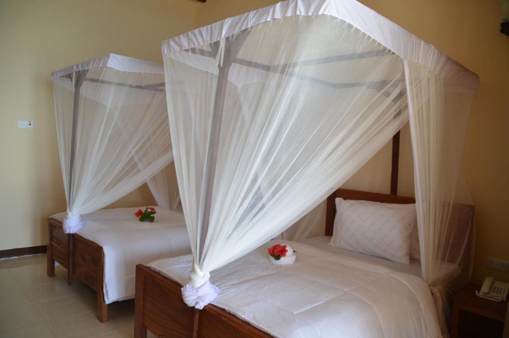 two beds in a room with white curtains and flowers at Sea View Beach Hotel in Zanzibar City