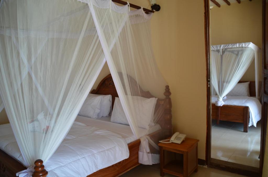 a bedroom with a bed with white curtains and a mirror at Sea View Beach Hotel in Zanzibar City