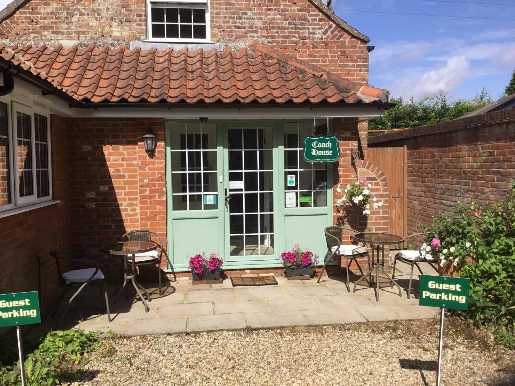 ein Backsteingebäude mit einer grünen Tür und Tischen und Stühlen in der Unterkunft Coach House Wroxham Holiday Cottage in Wroxham