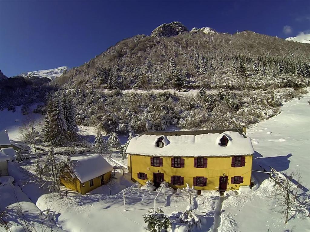 a yellow house with snow on it in front of a mountain at Gite Auberge Les Cascades in La Mongie