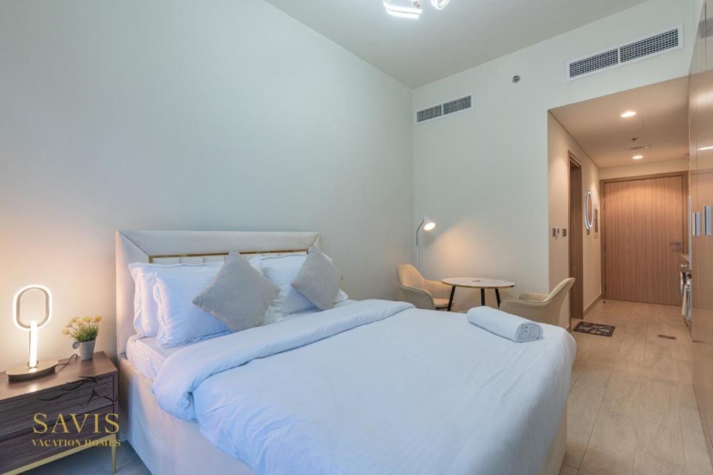 Un dormitorio con una gran cama blanca y una mesa. en Savis Homes - Azizi Riviera 43 - Chic Studio Near Downtown and Business Bay, en Dubái