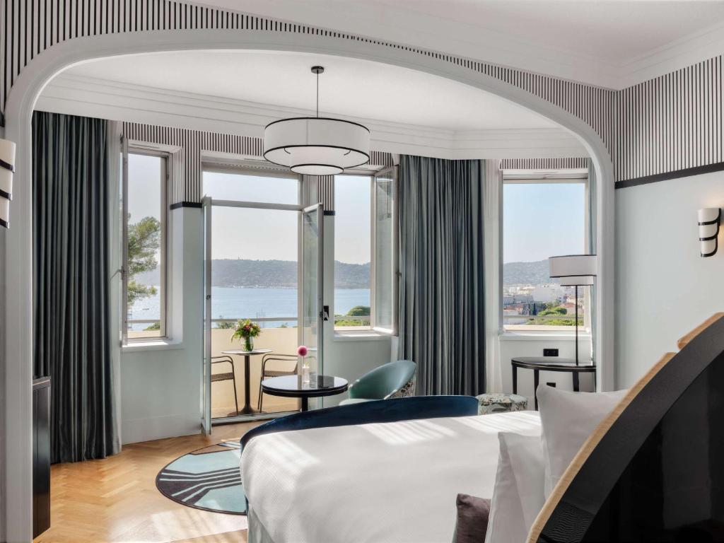 a hotel room with a bed and large windows at The 1932 Hotel & Spa Cap d'Antibes - MGallery Collection in Juan-les-Pins