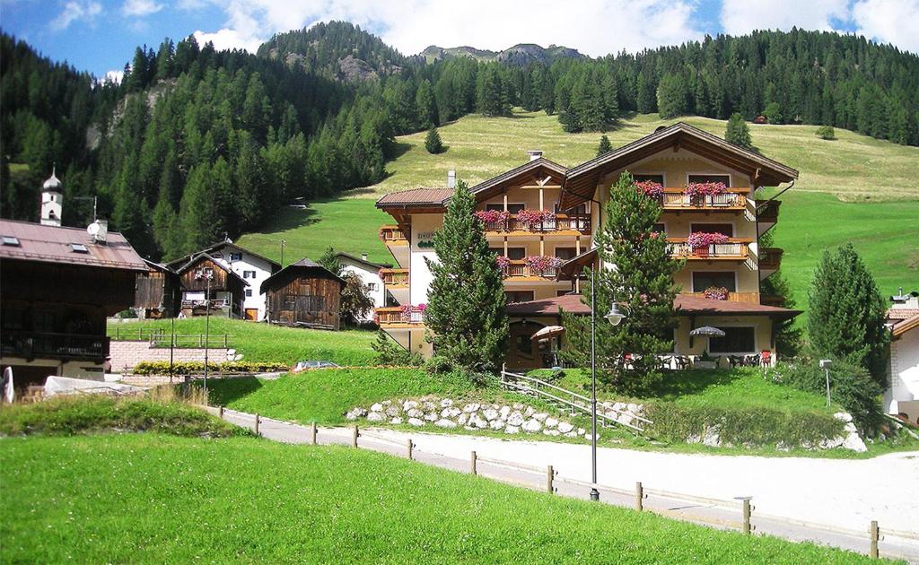 a large building on a hill next to a green field at Hotel Dolomites Inn in Canazei