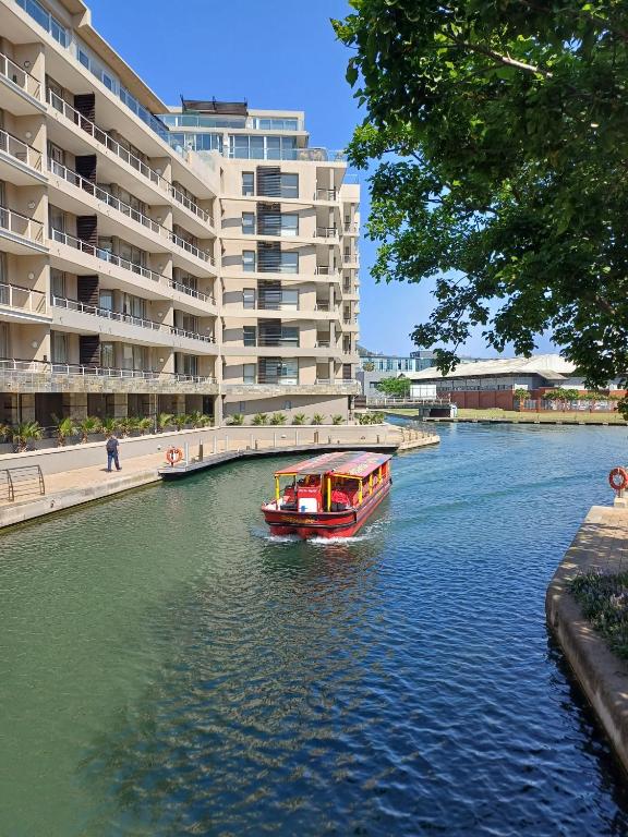 a boat in a river in front of a large building at Birds-eye canal view - Walk to CTICC and V&A Waterfront! in Cape Town
