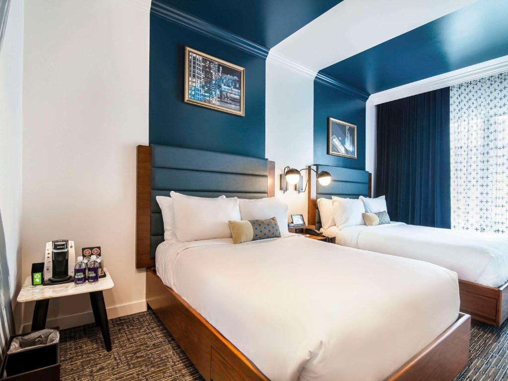 two beds in a hotel room with blue walls at Hotel Belmont Vancouver - MGallery Collection in Vancouver