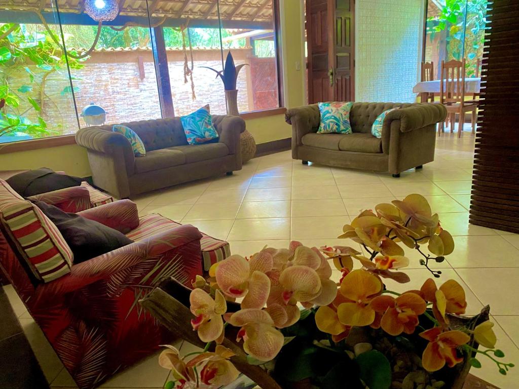 un salon avec des canapés et une plante avec des fleurs dans l'établissement Casa confortável e espaçosa em Búzios, à Armacao dos Buzios
