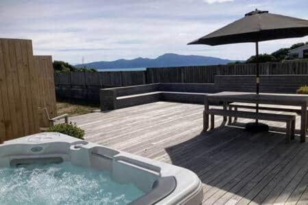 a hot tub with a picnic table and an umbrella at Seascapes Luxury Retreat in Paraparaumu