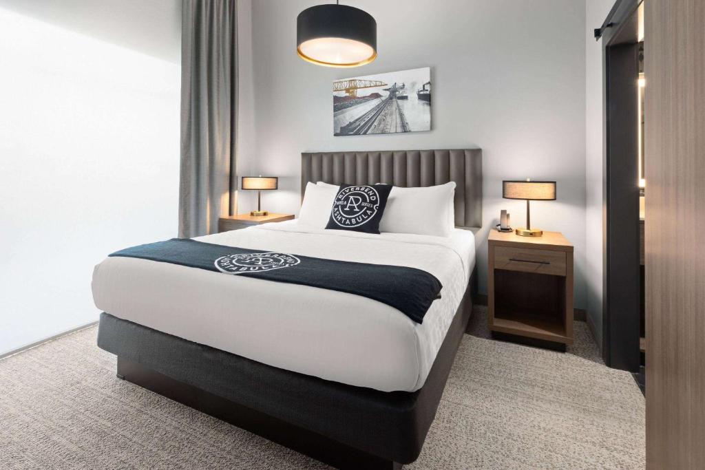 ein Schlafzimmer mit einem großen Bett und zwei Nachttischen und zwei Lampen in der Unterkunft Riverbend Hotel and Suites, Trademark Collection by Wyndham in Ashtabula