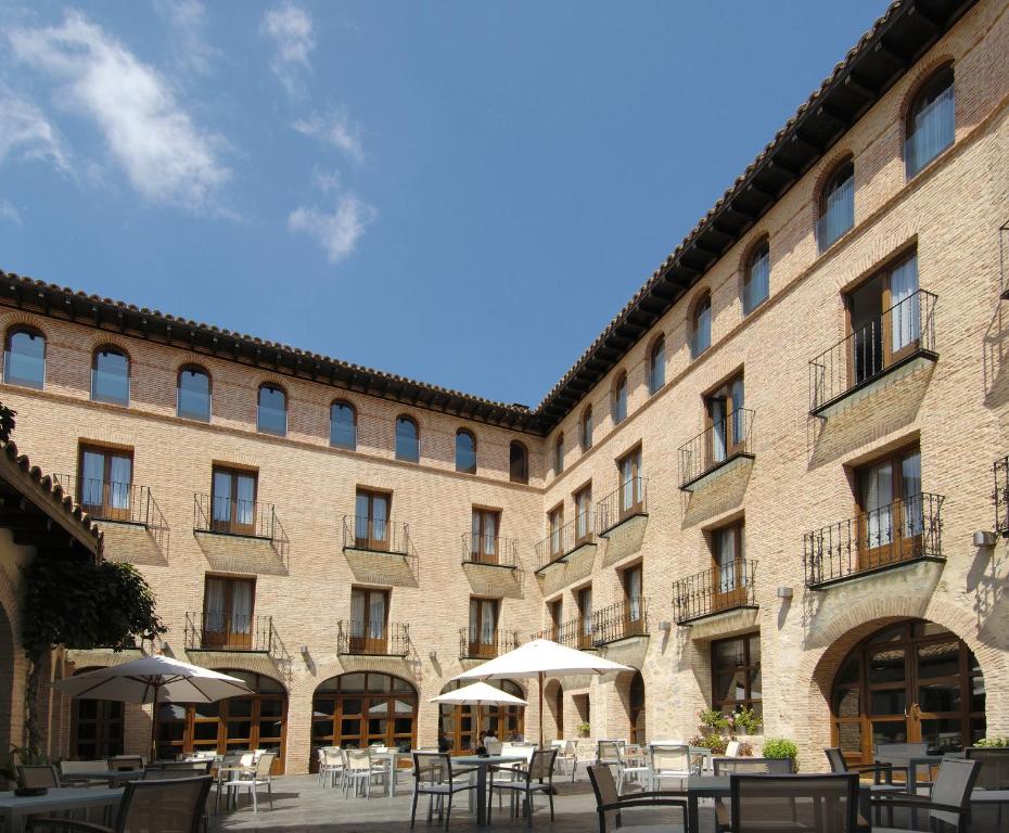 ein großes Backsteingebäude mit Tischen und Sonnenschirmen in der Unterkunft Hotel Cienbalcones in Daroca