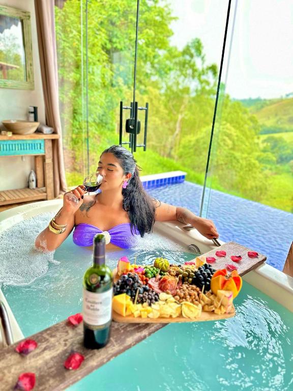a woman in a bath tub with a bottle of wine and food at Chalé Tucano super Luxo in Cunha