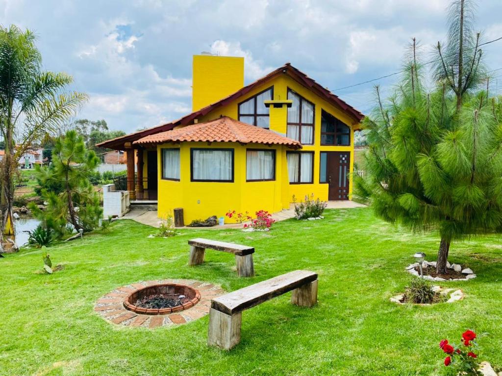 a yellow house with a fire pit in the yard at Cabañas Ojo de Agua in Mazamitla