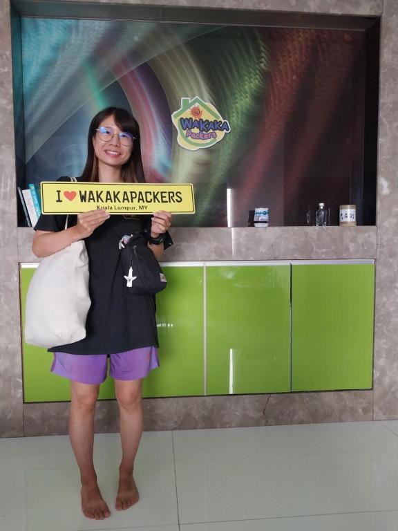a woman holding a sign in front of a wall at WakakaPackers in Kuala Lumpur
