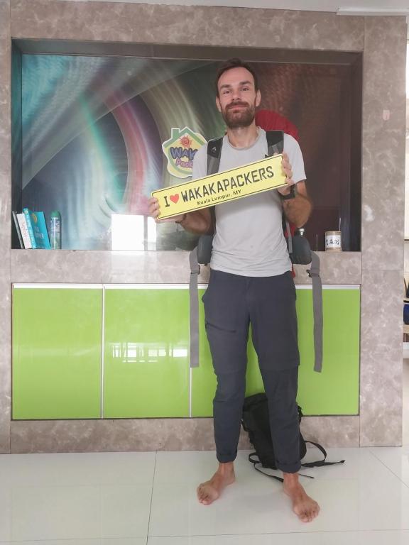 a man holding a sign in front of a counter at WakakaPackers in Kuala Lumpur