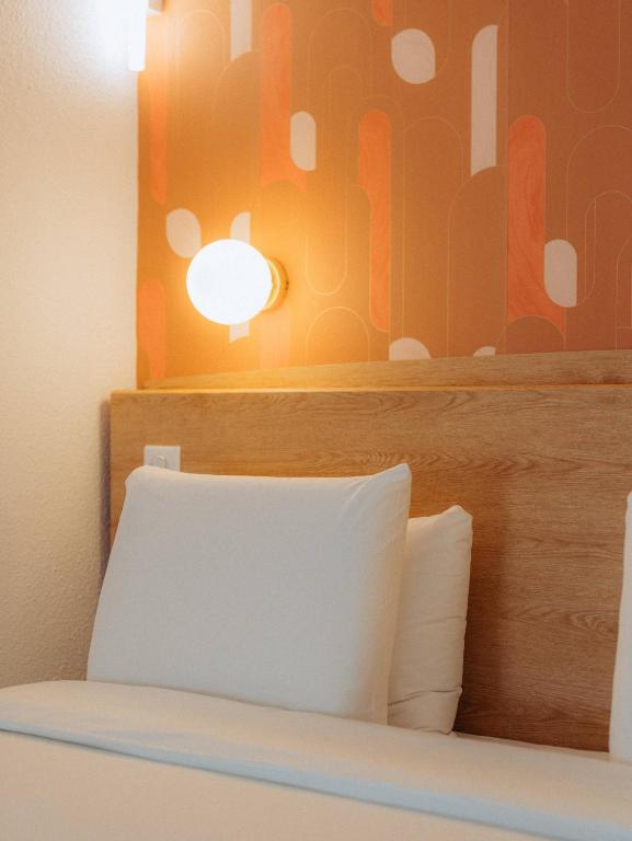 a bed with a wooden headboard with a light above it at Kyriad Cannes - Mandelieu in Cannes