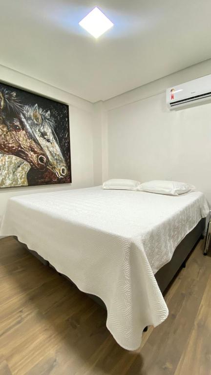 a white bed in a room with a painting on the wall at Hotel Zagonel in Chapecó